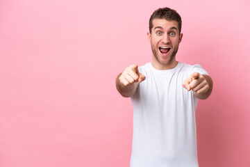 Young caucasian man isolated on pink background surprised and pointing front