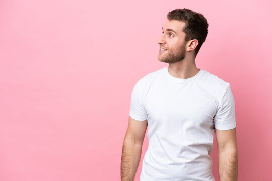 Young caucasian man isolated on pink background looking to the side and smiling
