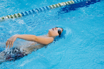 little caucasian boy wearing goggles swimming backstroke in a pool