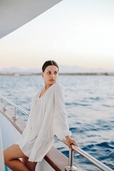 Portrait of a girl, in a white delicate dress, standing near the deck of the boat, against the background of the blue sea