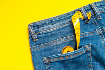 measuring tape is in the back pocket of blue jeans on a yellow background. The concept of tailoring, a clothing repair shop, the correct selection of clothing size.