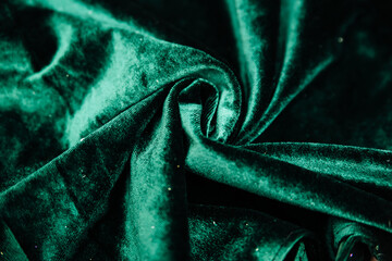 A green, wrinkled fabric lies in folds on a draped table. Emerald velvet.