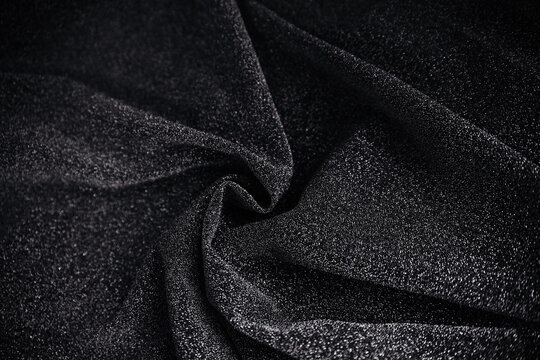 Black wrinkled fabric with sequins.Draped material. Glowing texture. Night sky