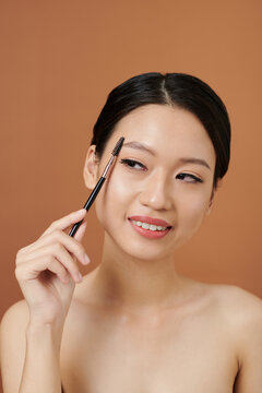 Studio portrait of smiling Vietnamese young woman brushing her eyebrows
