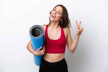 Young sport caucasian woman going to yoga classes while holding a mat isolated on white background smiling and showing victory sign