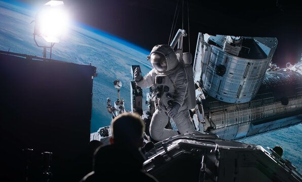 Behind the scenes of virtual production shot - Film crew working with Caucasian female astronaut stuntwoman in a spacesuit hanging on a wires against huge LED screen. Some elements furnished by NASA