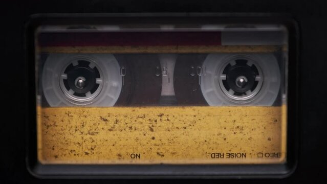 Vintage yellow audio cassette playing in a deck of an old tape recorder. Audiocassette with blank label in retro player spinning. Close-up. Call recording, retro playback, reel with tape rotating