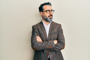 Middle age man with beard and grey hair wearing business jacket and glasses smiling looking to the side and staring away thinking.