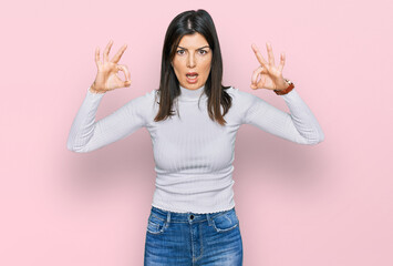 Beautiful brunette woman wearing casual clothes looking surprised and shocked doing ok approval symbol with fingers. crazy expression