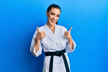 Beautiful brunette young woman wearing karate fighter uniform with black belt success sign doing positive gesture with hand, thumbs up smiling and happy. cheerful expression and winner gesture. © Krakenimages.com