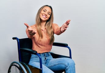 Beautiful hispanic woman sitting on wheelchair looking at the camera smiling with open arms for...