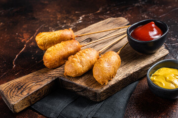 Traditional American street junk food Deep fried corn dogs with mustard and ketchup. Dark background. Top view