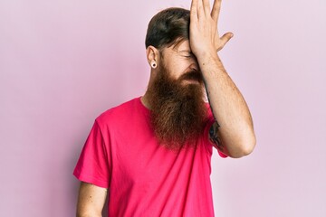 Redhead man with long beard wearing casual pink t shirt surprised with hand on head for mistake, remember error. forgot, bad memory concept.