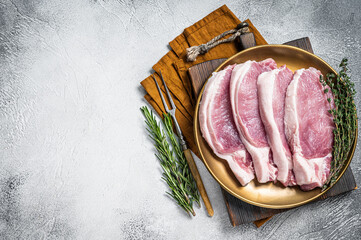 Fresh raw pork cutlet or chop steak on a plate with herbs. White background. Top view. Copy space