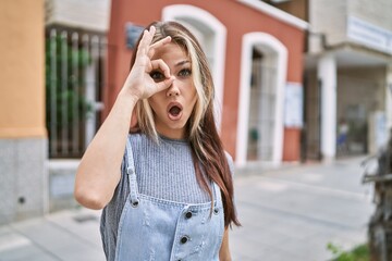 Fototapeta premium Young caucasian woman outdoors doing ok gesture shocked with surprised face, eye looking through fingers. unbelieving expression.