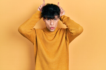 Handsome hipster young man wearing casual yellow sweater doing funny gesture with finger over head...