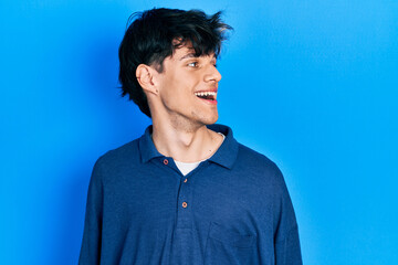 Handsome hipster young man stranding over blue background looking away to side with smile on face, natural expression. laughing confident.