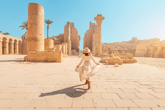 Happy woman traveler explores the ruins of the ancient Karnak temple in the heritage city of Luxor in Egypt. Giant row of columns with carved hieroglyph