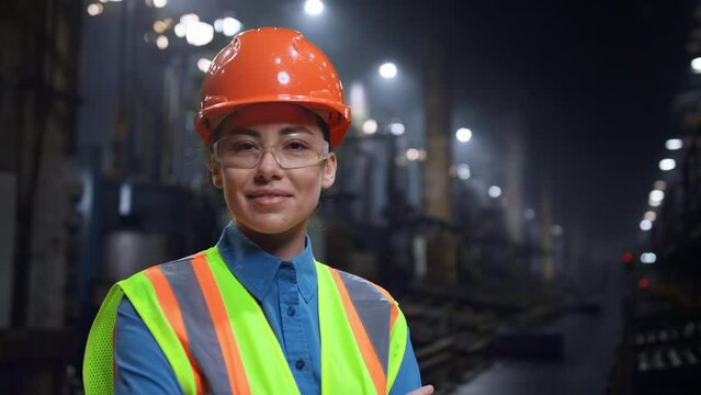 Woman engineer smiling camera wearing safety helmet at huge industrial storage.