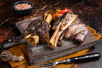 Traditionally slow cooked Leg of Lamb or Lamb Shank with vegetables on a cutting board. Dark background. Top view