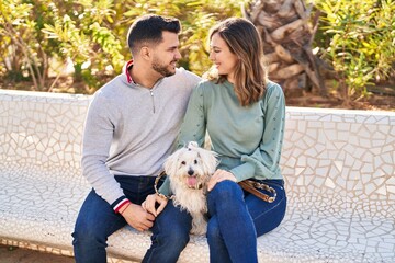 Man and woman holding dog hugging each other at park