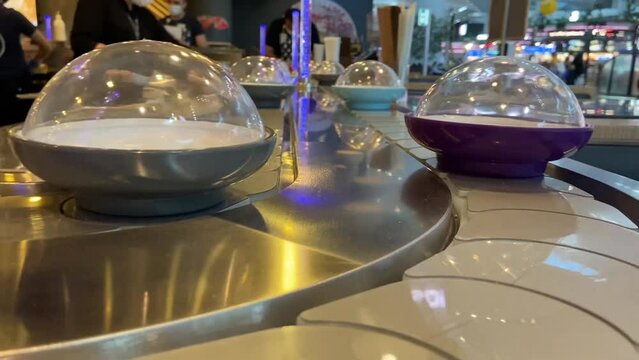 Close-up dishes are on conveyor or belt buffet in self-service restaurant, kaiten sushi bar inside. Chefs cooking food on background. Self service