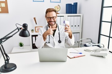 Middle age doctor man holding thermometer at the clinic smiling happy pointing with hand and finger