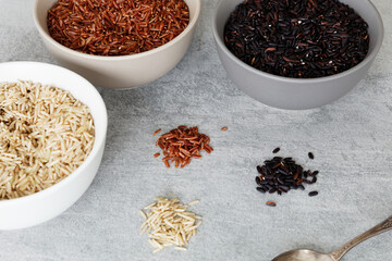 Rice of different colors: brown, red and black in a bowl and heaps on a table.