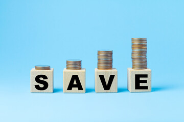 Stack of coins are placed on 4 wooden cubes with the word "SAVE" on a blue background. Ideas for saving money for the future.