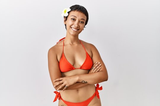 Young hispanic woman with short hair wearing bikini happy face smiling with crossed arms looking at the camera. positive person.