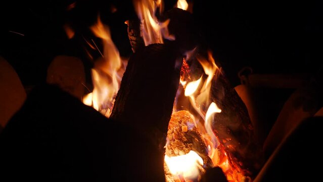 Campfire burning and glowing nicely in the dark. Firewood stacked in a fire pit with flames.  