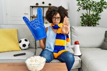 African american woman with afro hair wearing team scarf cheering game holding megaphone with open hand doing stop sign with serious and confident expression, defense gesture