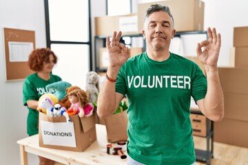 Obraz premium Middle age man wearing volunteer t shirt at donations stand relax and smiling with eyes closed doing meditation gesture with fingers. yoga concept.
