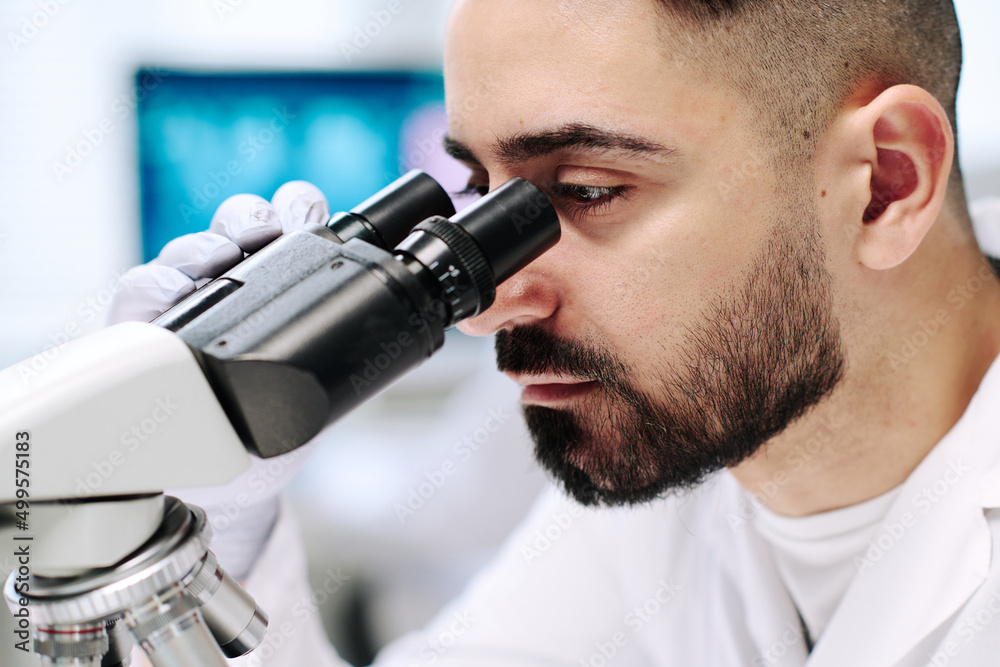 Poster part of face of young male researcher with microscope studying new virus while sitting by workplace 