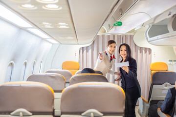 Happy Asian woman traveler standing and holding boarding pass while Flight attendant is checking passenger boarding pass in business class and show the way to her seat for airplane flight. Copy space