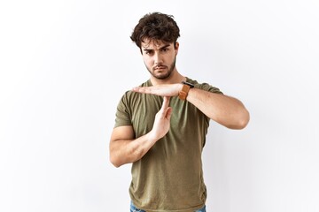 Hispanic man standing over isolated white background doing time out gesture with hands, frustrated...