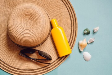 Summer beach essentials, sea travel concept. Sun hat, sunglasses, yellow sunscreen bottle and seashells flat lay photography