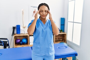 Young african american woman working at pain recovery clinic with hand on head for pain in head because stress. suffering migraine.