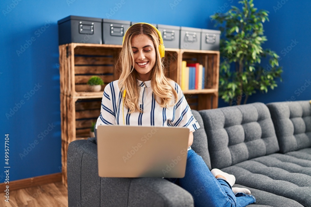 Wall mural Young blonde woman listening to music sitting on sofa at home