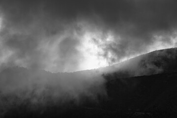 a black and white picture taken from the mountain down through the clouds to the shining atlantic ocean. Madeira, Portugal