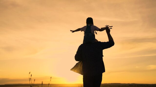 Kid, pilot sits on his dads shoulders in pilots goggles. Teamwork father, child, family dream to fly. Happy family, dad, kid daughter play together with toy plane against background of spring sky.