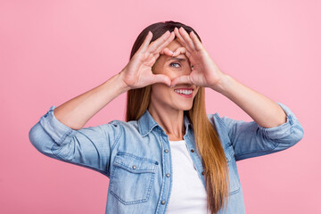 Photo of young cheerful woman show fingers heart shape watch eye cupid romance isolated over pink color background