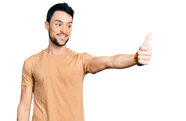 Hispanic man with beard wearing casual t shirt looking proud, smiling doing thumbs up gesture to the side