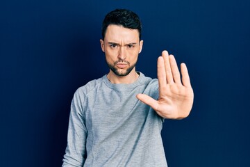 Young hispanic man wearing casual clothes doing stop sing with palm of the hand. warning expression...