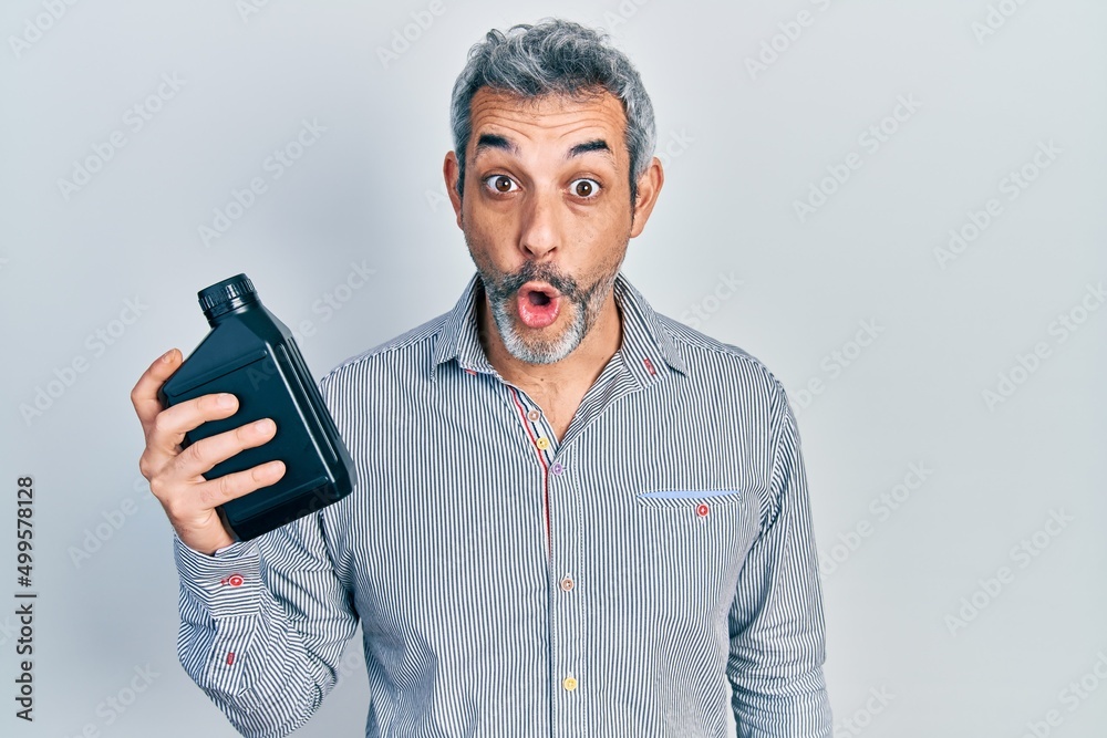 Sticker handsome middle age man with grey hair holding motor oil bottle scared and amazed with open mouth fo