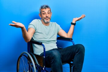 Handsome middle age man with grey hair sitting on wheelchair clueless and confused expression with...