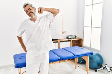 Middle age hispanic therapist man working at pain recovery clinic stretching back, tired and relaxed, sleepy and yawning for early morning