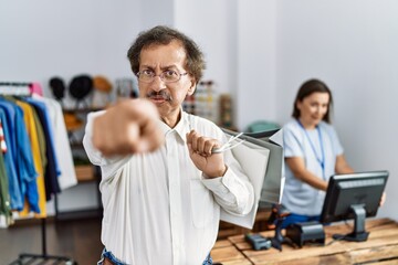 Southeast asian man wearing holding shopping bags pointing with finger to the camera and to you, confident gesture looking serious