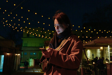 Portrait of a young smiling woman looking at her phone in a night city