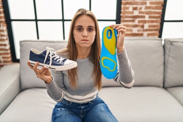 Young woman holding shoe insole puffing cheeks with funny face. mouth inflated with air, catching...